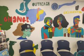 Indoor illustration on wall of people made up of colorful patches of yellow, green, brown, blue, and red with words "Change," "Outreach," and "Collaboration" in bubble letters.