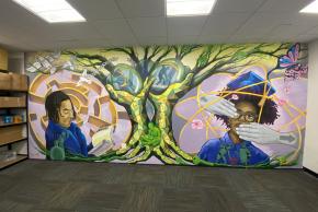 Finished indoor mural at Brooklyn Justice Initiatives featuring illustrations of two students amid imagery of trees, birds, and butterflies.