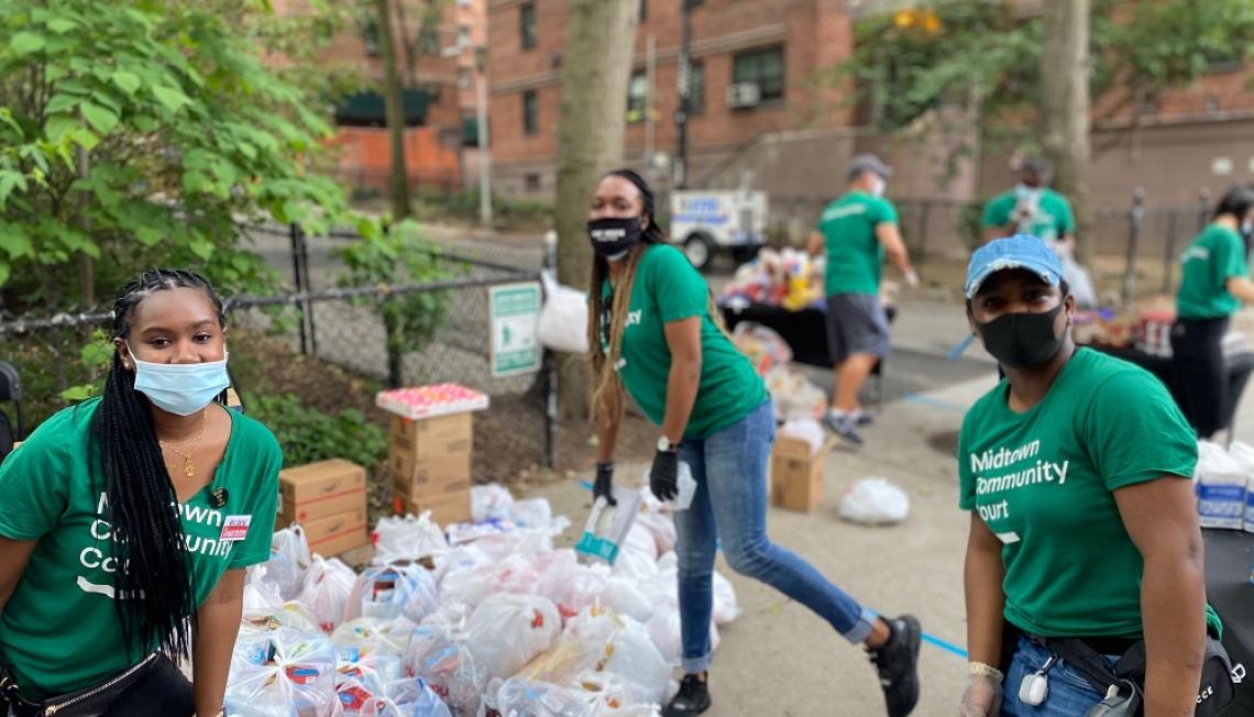 Three women in masks and green t-shirts that say Midtown Community Court distribute supplies to the community
