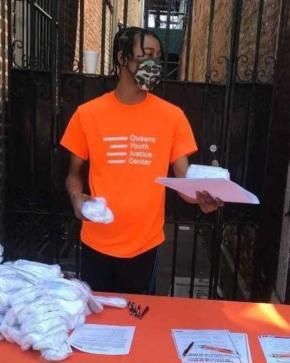 A young man in a Queens Youth Justice Center t-shirt hands out supplies