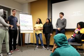 Joe Barrett standing up with a group of youth participants in presentation in front of a whiteboard