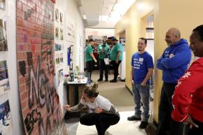 staff from various programs participating in an art activity in the office. Staff standing and talking while one draws on the graffiti wall. 
