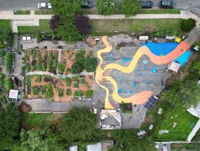 Overhead shot of community garden with mural on the pavement, featuring squiggly rays of yellow emanating from sun illustration on the garden's border.